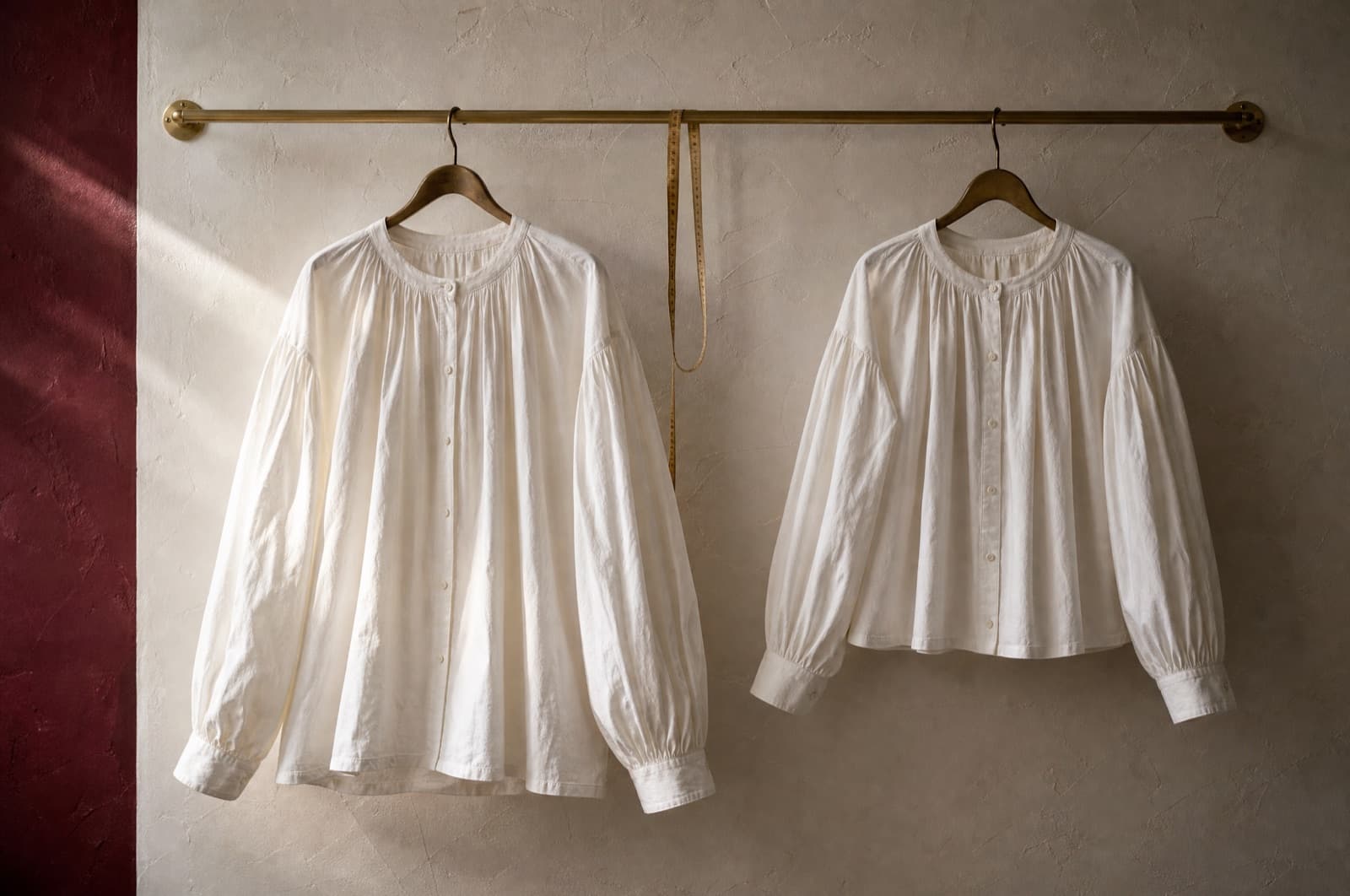 The same blouse in two sizes hung side by side with a measuring tape between them.