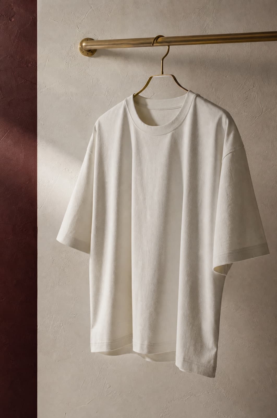 Boxy Cotton Tee, hung from a rail against limestone plaster.