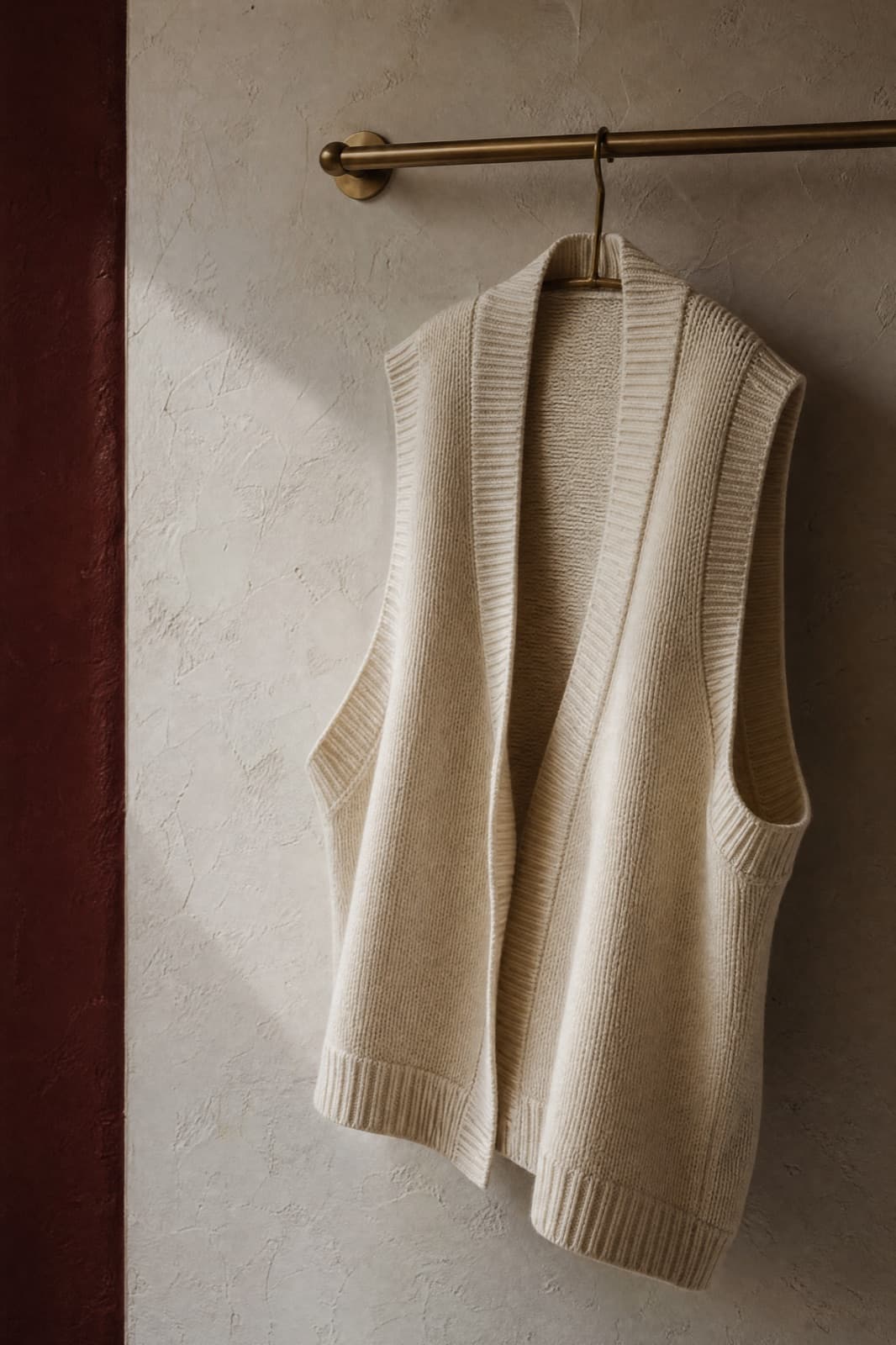 Cotton Knit Vest, hung from a rail against limestone plaster.