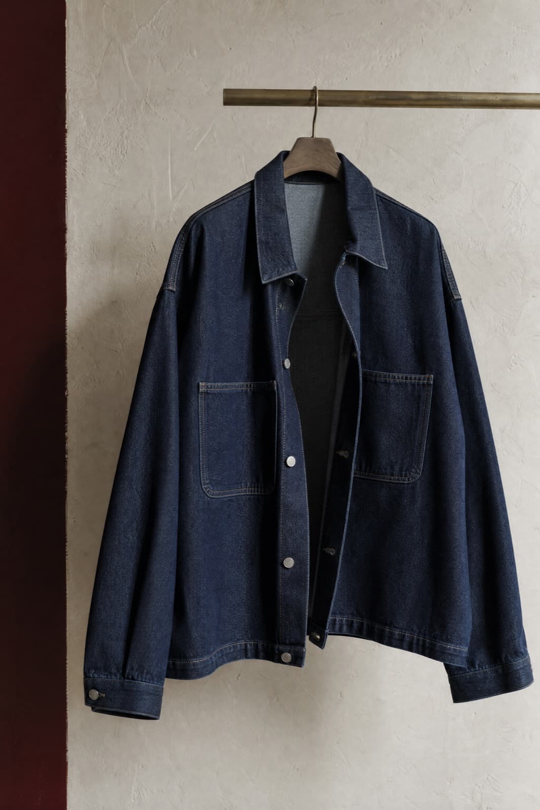 Denim Jacket Oversized, hung from a rail against limestone plaster.