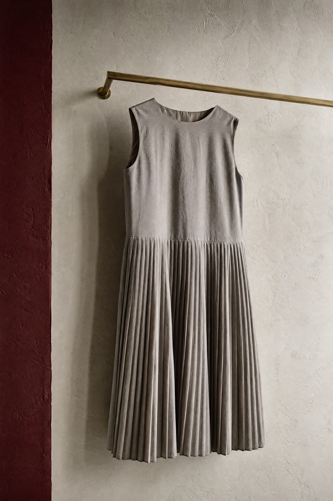 Pleated Midi Dress, hung from a rail against limestone plaster.