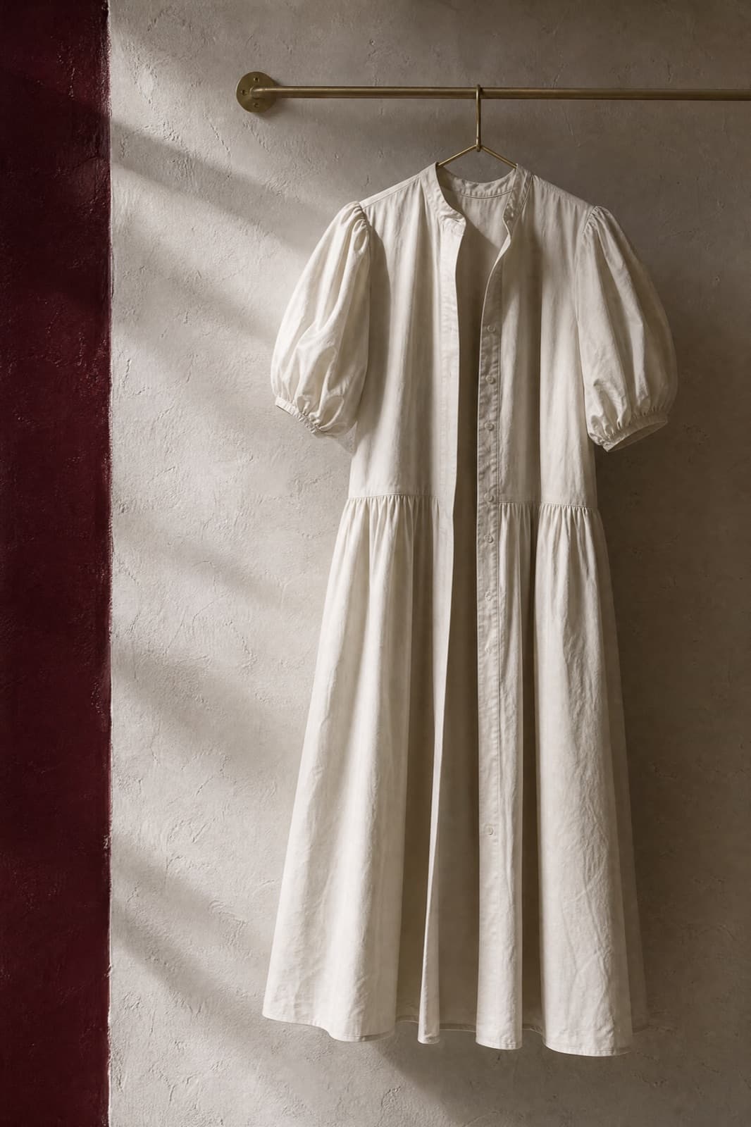 Puff-Sleeve Cotton Dress, hung from a rail against limestone plaster.