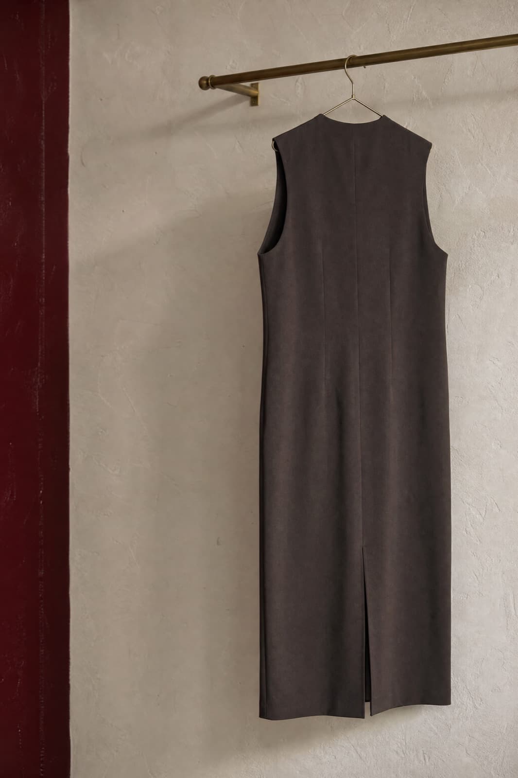 Sleeveless Column Dress, hung from a rail against limestone plaster.