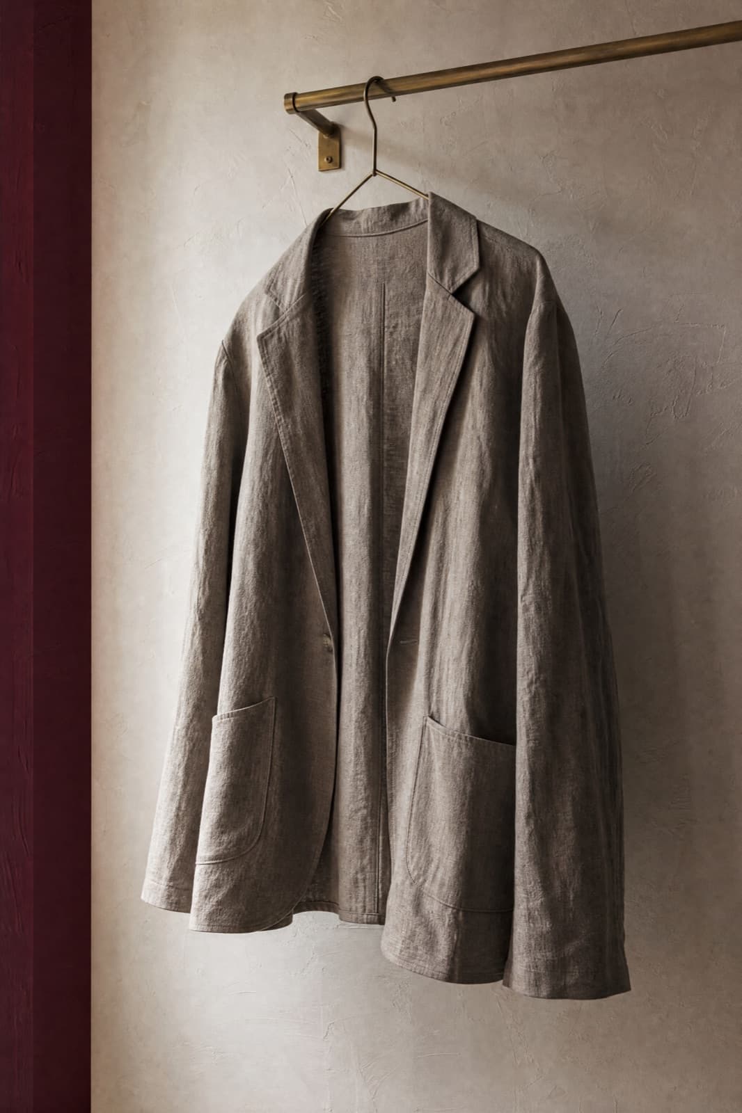 Unstructured Blazer, hung from a rail against limestone plaster.