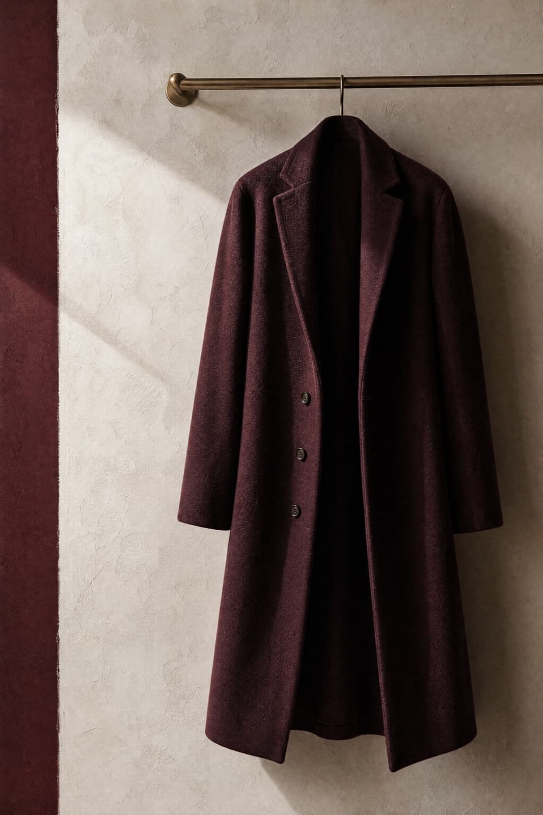 Wool-Blend Coat, hung from a rail against limestone plaster.